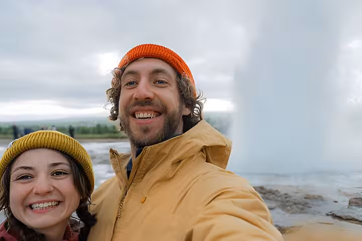 Smiling couple taking selfie in front of erupting geyser on Golden Circle tour in Iceland