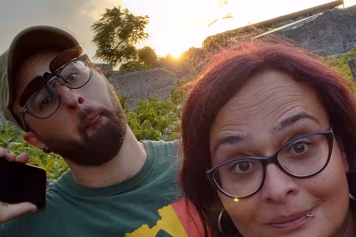 Two travelers with glasses taking a selfie at sunset near ancient Pompeii ruins and greenery