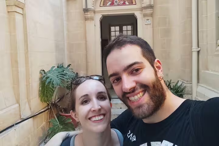 Smiling couple taking a selfie in front of a historic stone building in Valletta, Malta