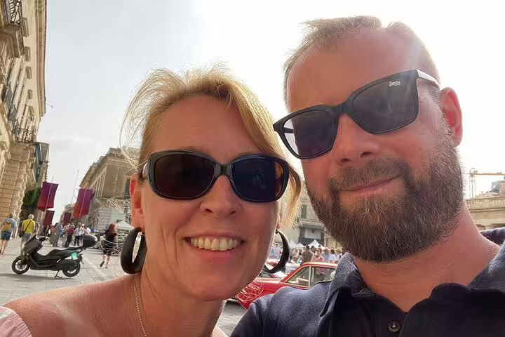 Couple smiling in sunglasses on a sunny Valletta street with historic buildings