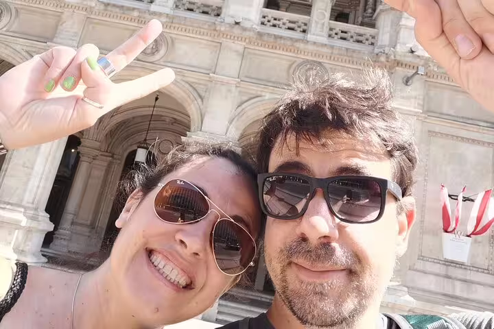 Couple taking a selfie with peace signs in front of a historic Vienna building on a walking tour