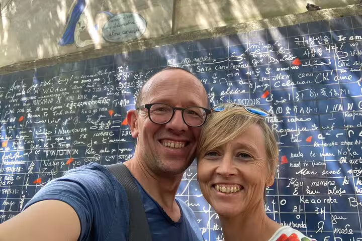 Couple smiling in selfie in front of the Wall of Love in Montmartre, Paris