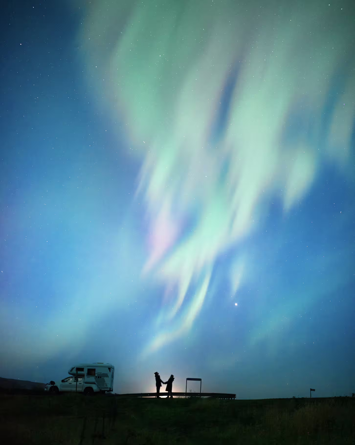 Couple silhouetted beneath vibrant green and pink aurora borealis dancing over Iceland on a private northern lights photography tour