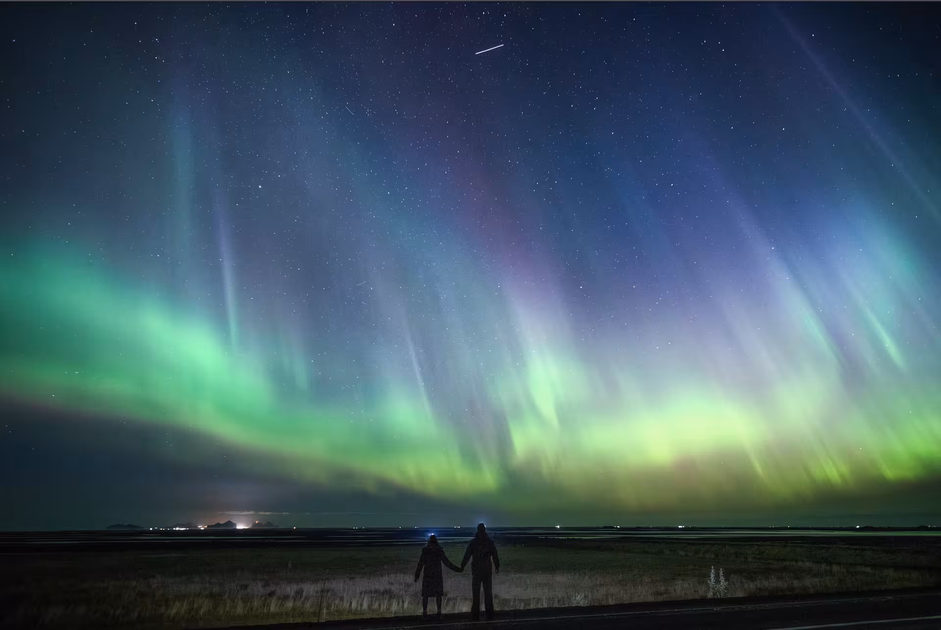 Couple holding hands silhouetted against a stunning multicolored northern lights display in Iceland night sky