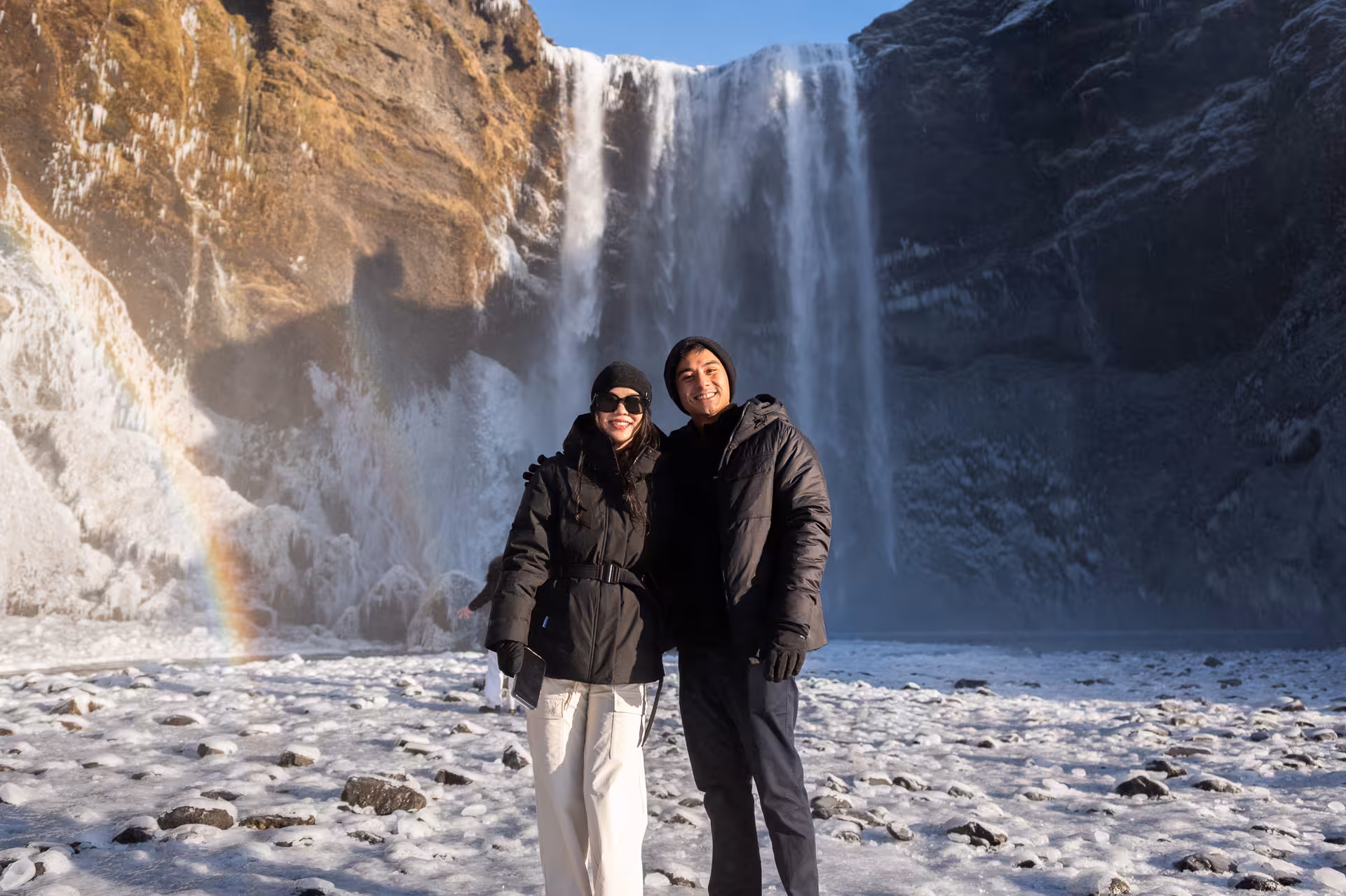 Couple posing in front of Skógafoss waterfall with rainbow on Iceland South Coast winter tour