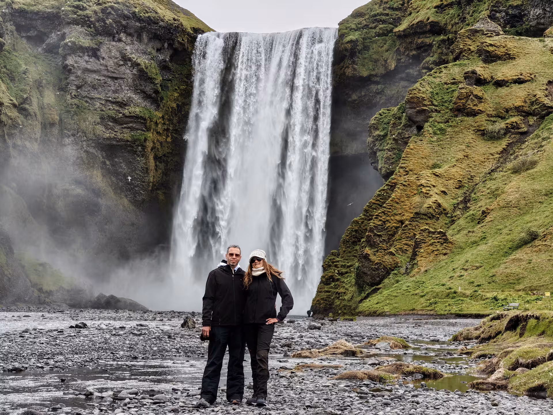 Couple standing in front of Skógafoss waterfall on Iceland's South Coast, surrounded by green mossy cliffs