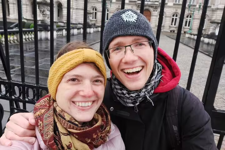 Smiling couple on Brussels walking tour posing in front of historic building iron gates