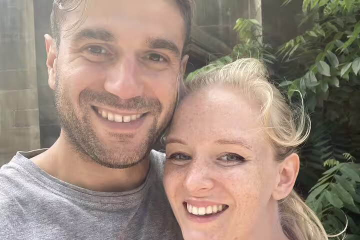 Smiling couple posing together outdoors surrounded by green tropical foliage