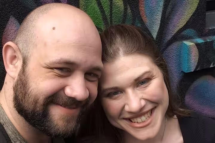 Smiling couple posing together in front of a colorful street art mural in Ottawa
