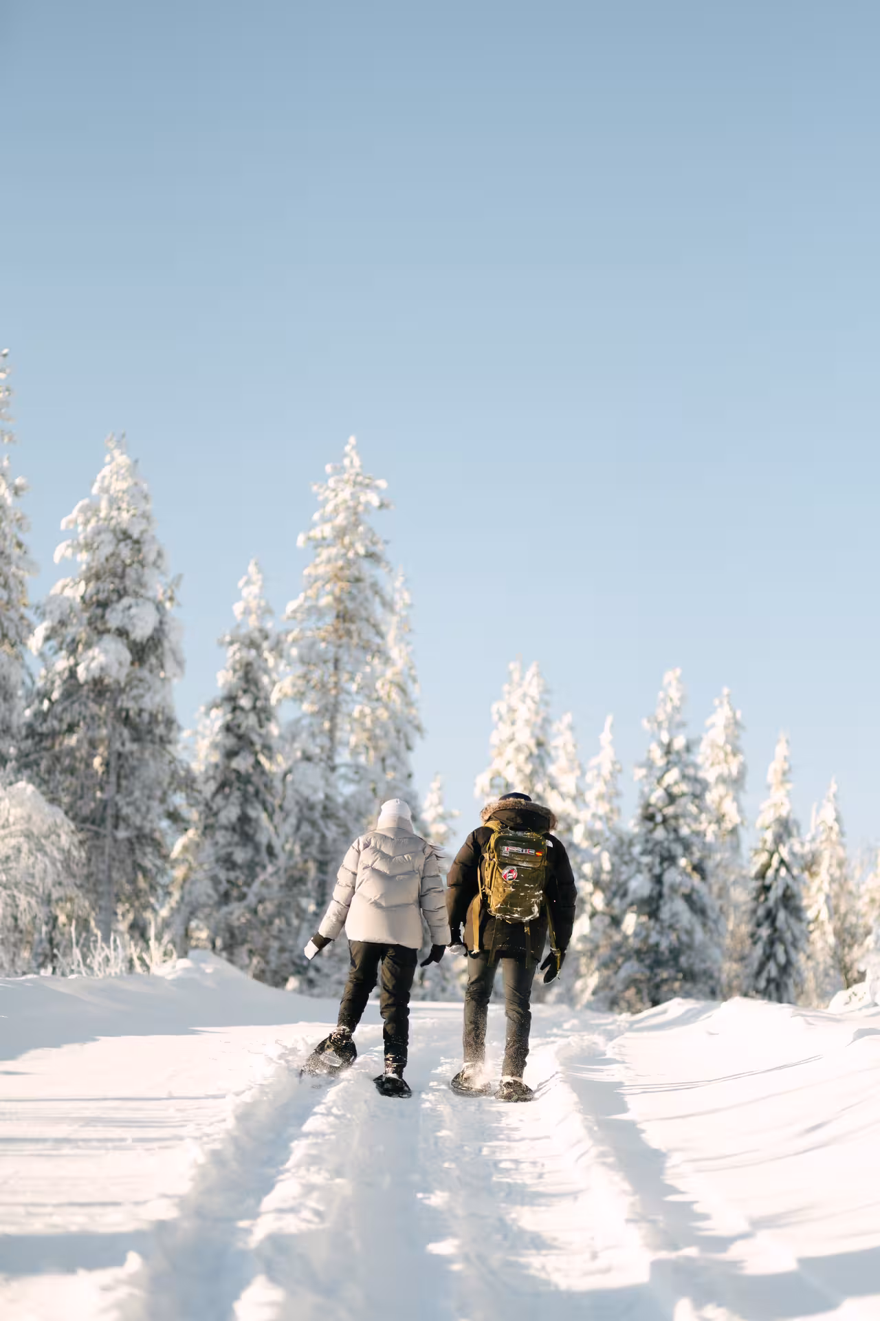 Couple snowshoeing through a snowy forest in Rovaniemi, enjoying a private holiday photo session.