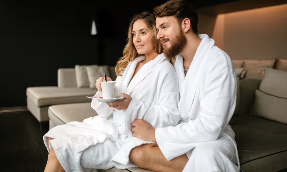 Couple in white bathrobes relaxing on a luxury spa sofa during an overnight wellness and dinner escape in Castellammare