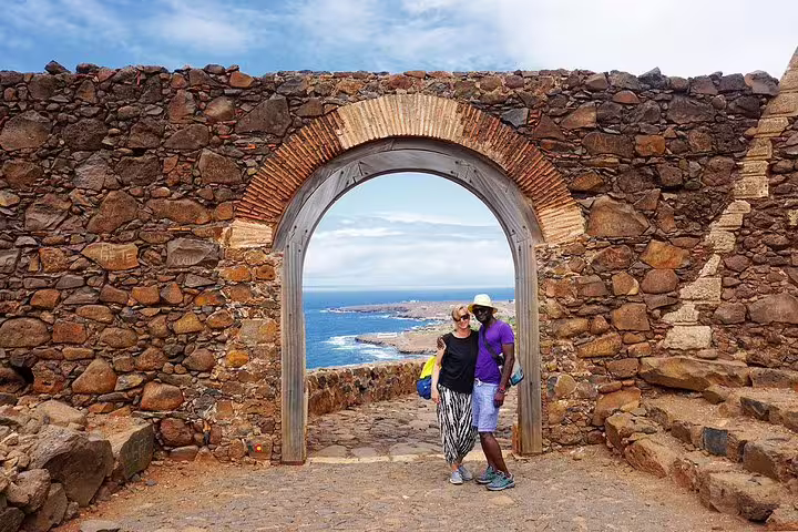 Couple stands under stone archway at Cidade Velha, overlooking Praia’s stunning coastline on Like Locals tour.