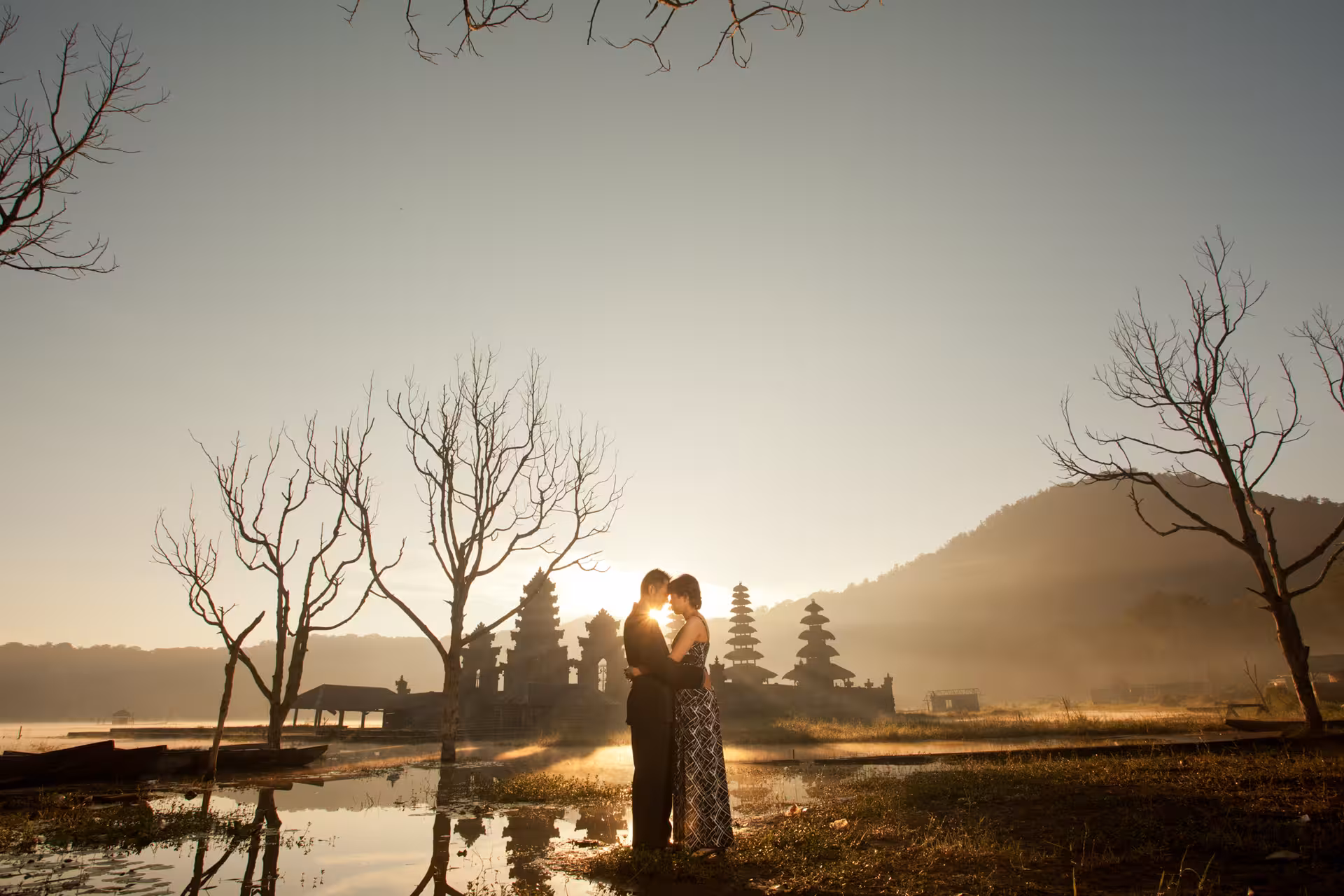 Couple embracing at sunset near Bali temple, creating a romantic silhouette during a private photoshoot.