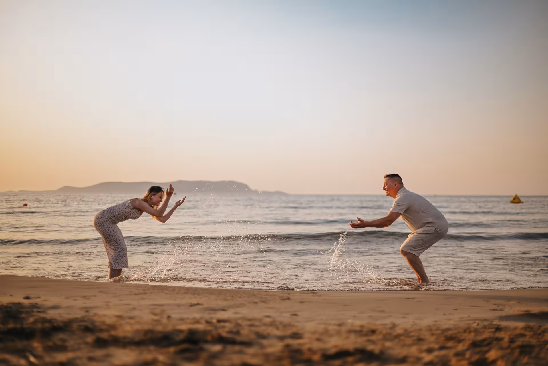 Couple enjoying a playful moment by the sea in Analipsi during a private beach photoshoot at sunset.