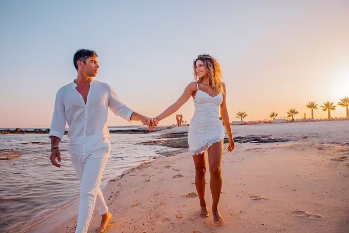 Couple walks hand in hand on Ayia Napa beach at sunset, captured during a professional photoshoot.