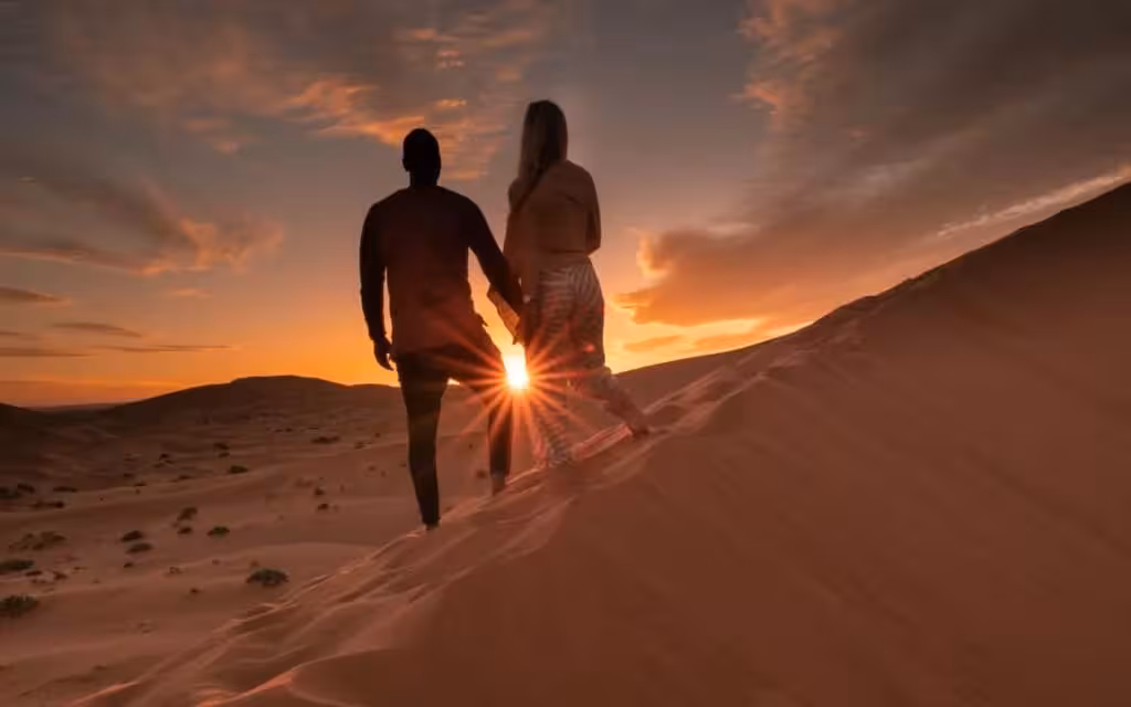 Couple holding hands at sunset on a sand dune during 4-day Merzouga Sahara desert tour from Fes.