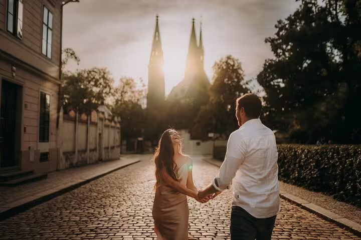 Couple laughs and holds hands on a cobblestone street in Prague at sunset, perfect for a photoshoot experience.