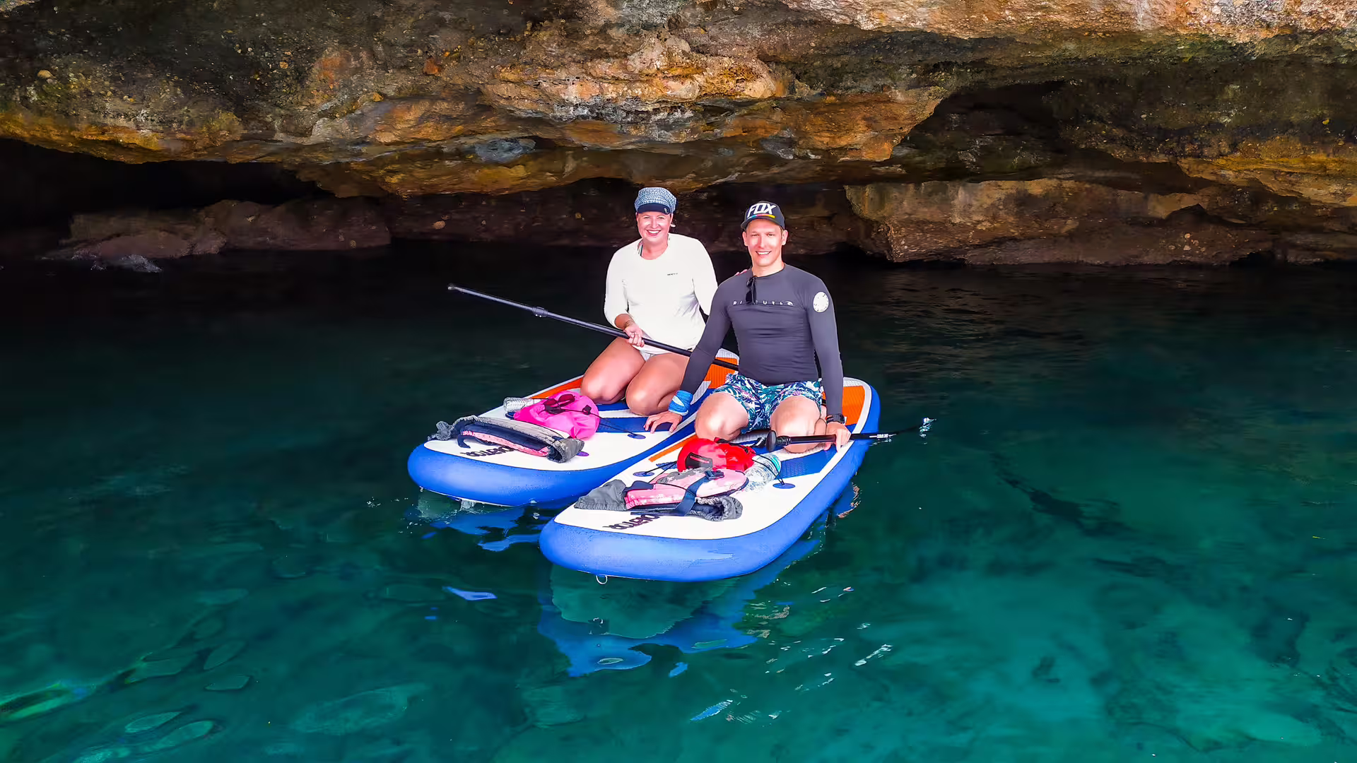 Couple on SUP boards in a sea cave near Kalamata, paddling over crystal-clear water on a guided tour