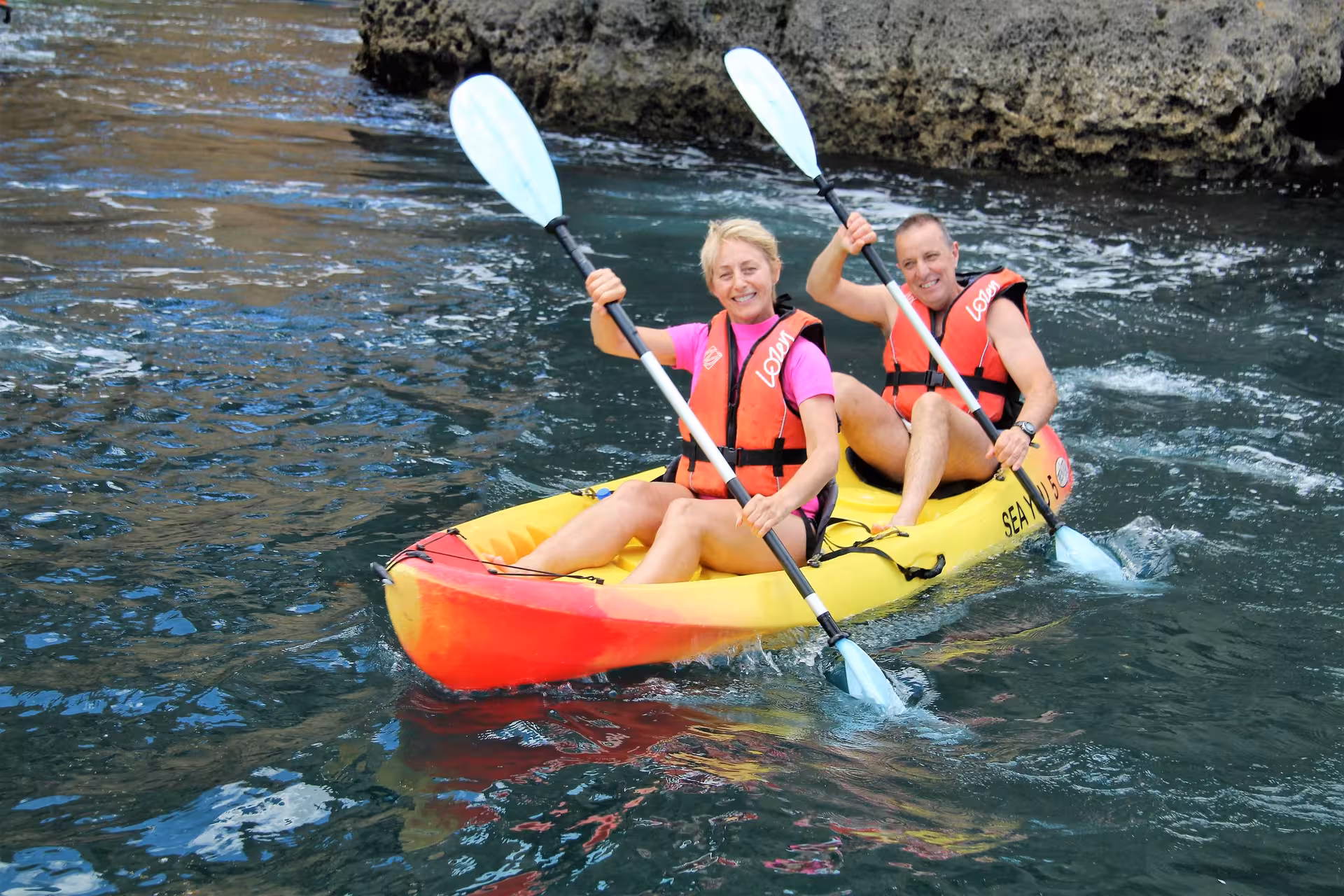 Couple enjoying guided kayak tour in Lagos, Portugal, paddling a tandem kayak through clear blue Atlantic waters