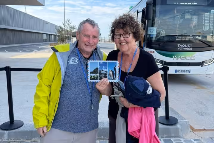Smiling couple holding a postcard in front of a Taquet Voyages tour bus in Honfleur