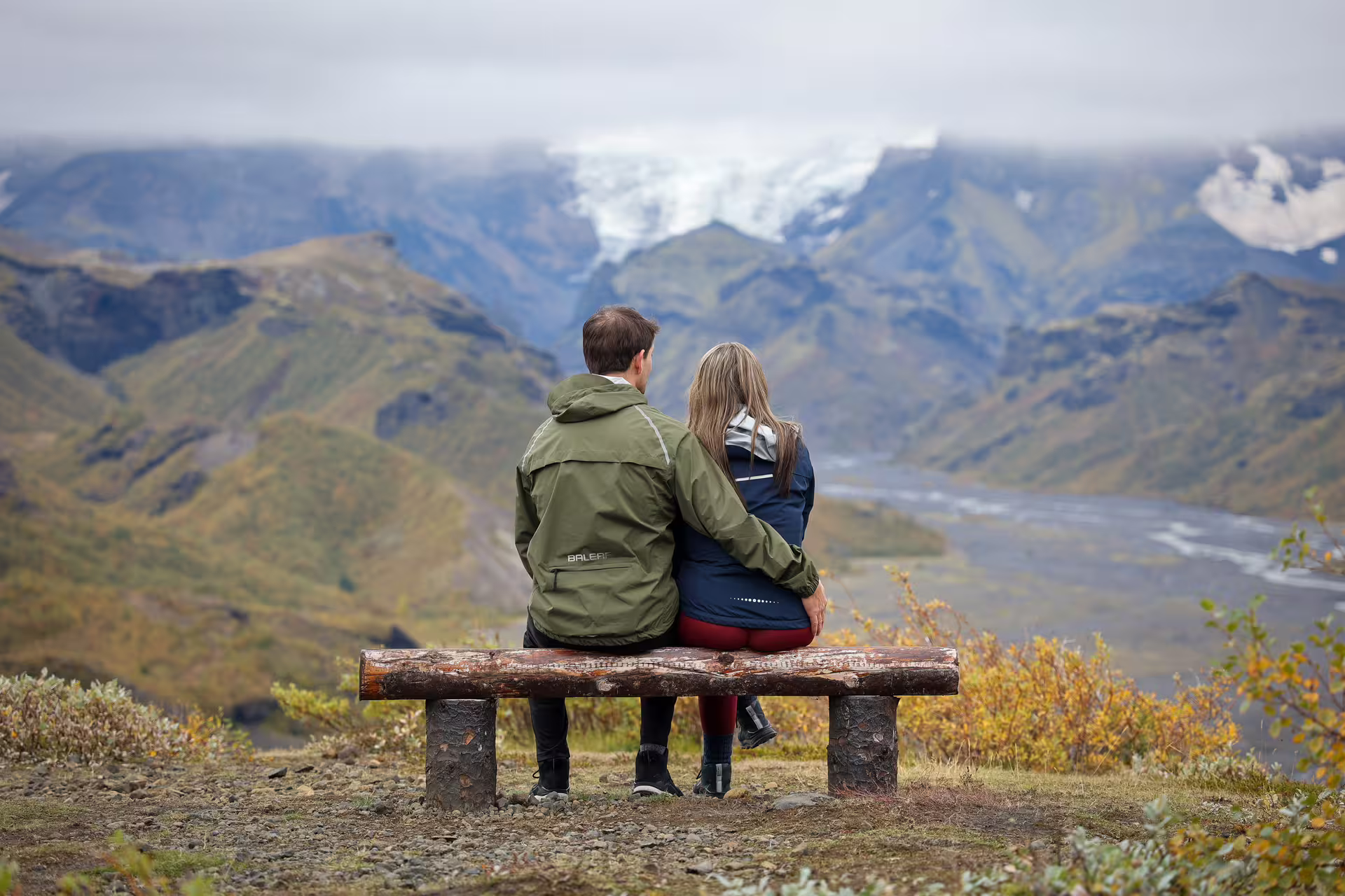 Couple sitting on a wooden bench enjoying breathtaking Thorsmork glacier valley views on a full-day 4x4 tour from Reykjavik Iceland