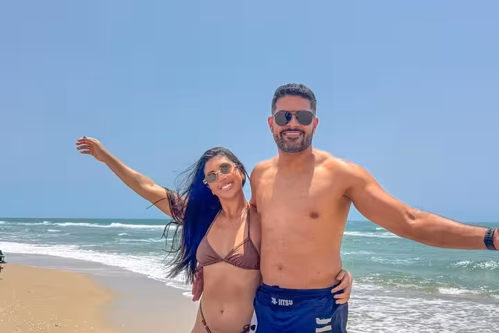 Couple posing on sunny shoreline with waves, enjoying a 3 beaches in 1 day beach tour in Ceará