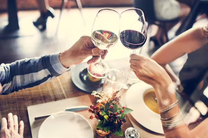 Couple toasting with glasses of red and white wine over an elegant local lunch during a private winery tour.
