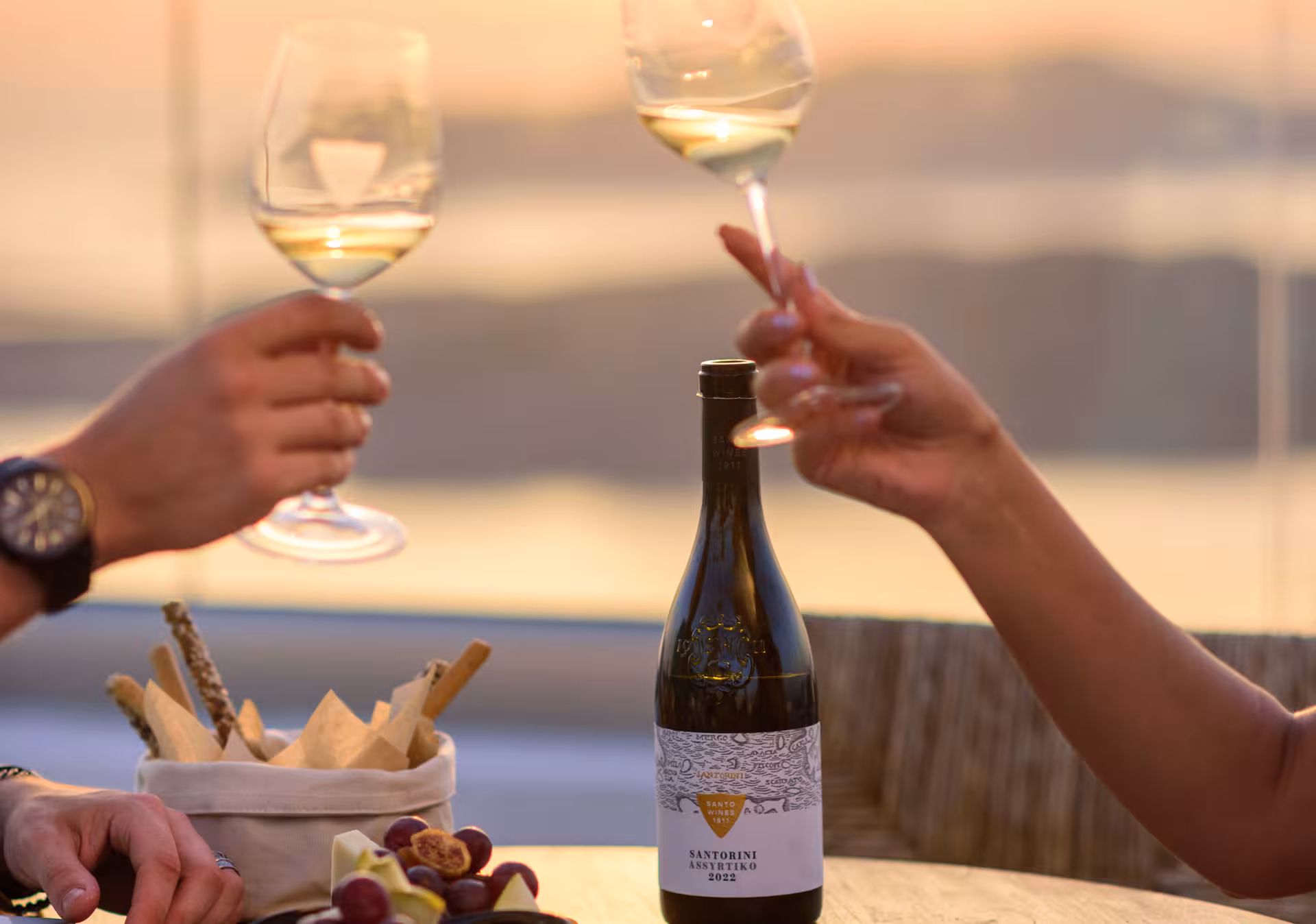 Couple toasting Santorini Assyrtiko at sunset during Santo Winery dinner, with local bites and caldera view