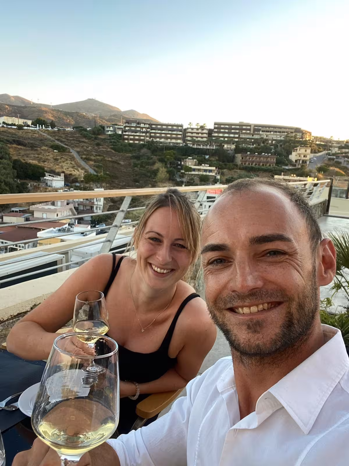 Couple toasting with white wine during an eco bike wine tour tasting, with scenic hillside town views at sunset