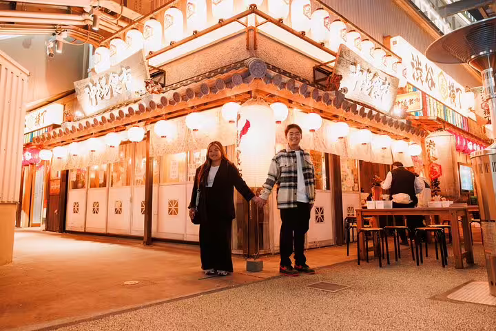 Couple holding hands outside lantern-lit izakaya in Tokyo, personal vacation photographer tour evening shoot