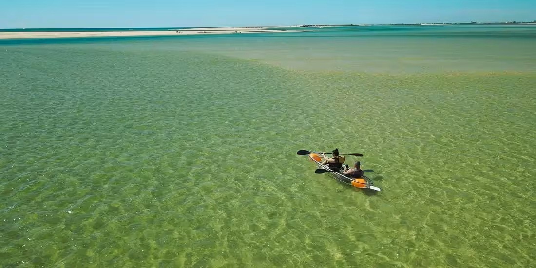 Couple in a transparent kayak gliding over shallow crystal-clear lagoon near sandbar on a 4-hour rental