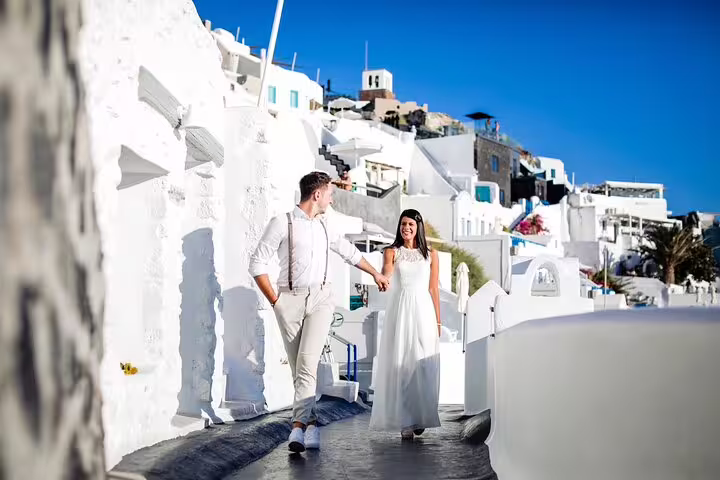 Couple walking in Oia Santorini, engagement photographer capturing romantic proposal shoot by whitewashed villas