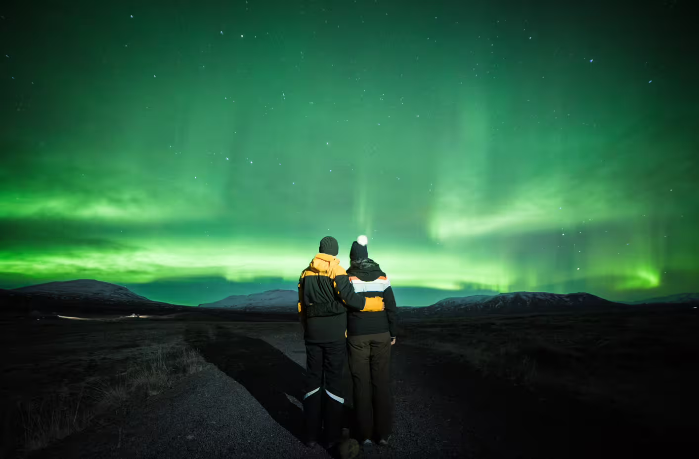 Couple embracing under vibrant green Northern Lights aurora borealis over Iceland landscape at night