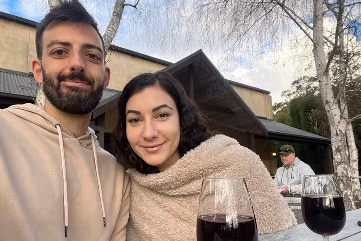 Couple enjoying wine tasting at a Southern Highlands winery with two glasses of red wine on an outdoor table.