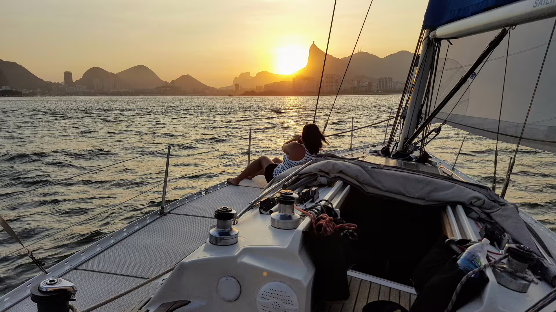 Couple relaxing on a yacht at sunset with panoramic views of Rio de Janeiro's skyline and mountains.