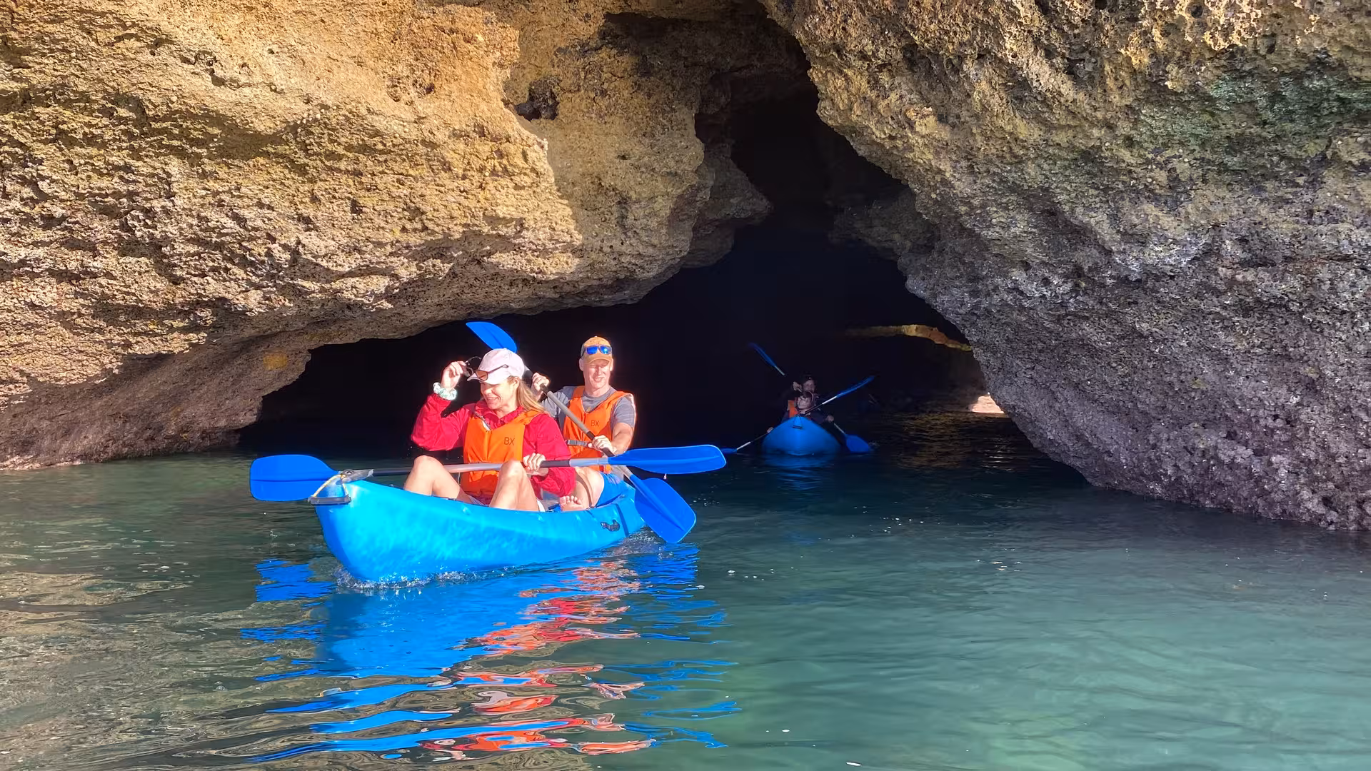 Couples kayaking into a rocky sea cave near Benagil, exploring hidden Algarve grottoes on a guided kayak experience