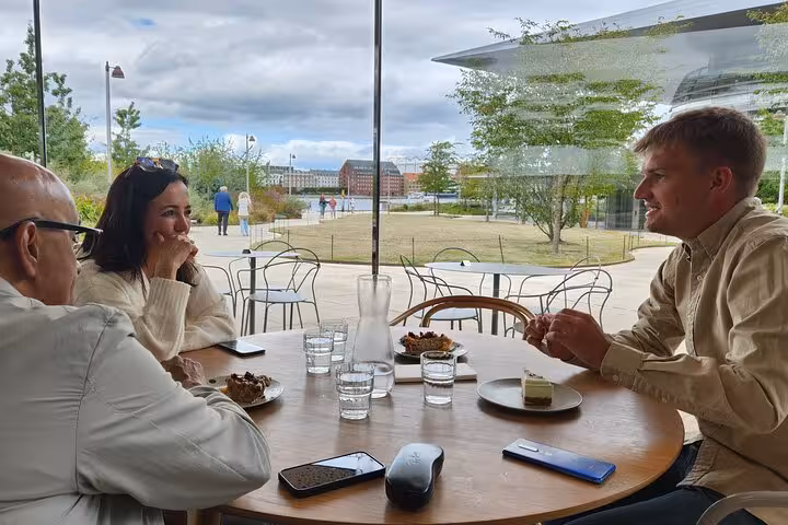 Delightful outdoor cafe setting with coffee and cake, overlooking modern architecture and lush greenery.