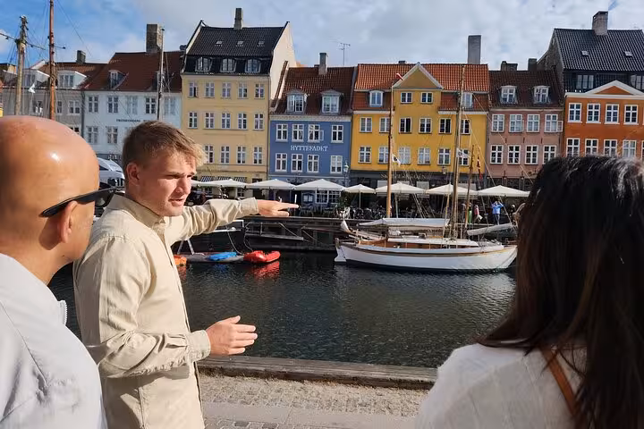 Tour guide points out colorful historic buildings and boats along a bustling canal, enhancing the cultural walking tour vibe.