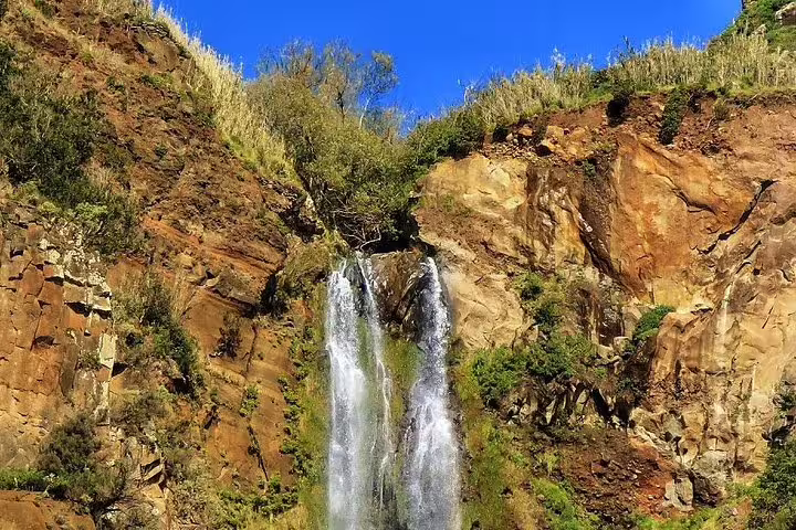 Scenic waterfall cascading down rocky cliffs under a clear blue sky, featured on the Craters of Fire 4X4 Full-Day Tour.