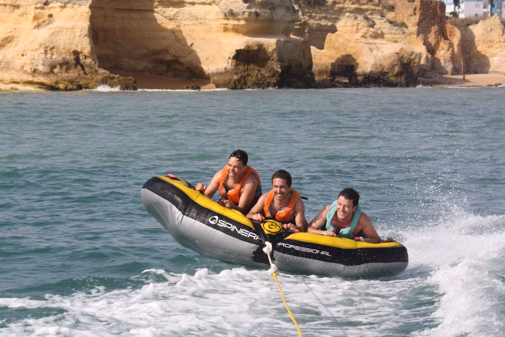 Three friends laughing on a Crazy Cookie inflatable tube ride along the Algarve rocky coastline watersport tour