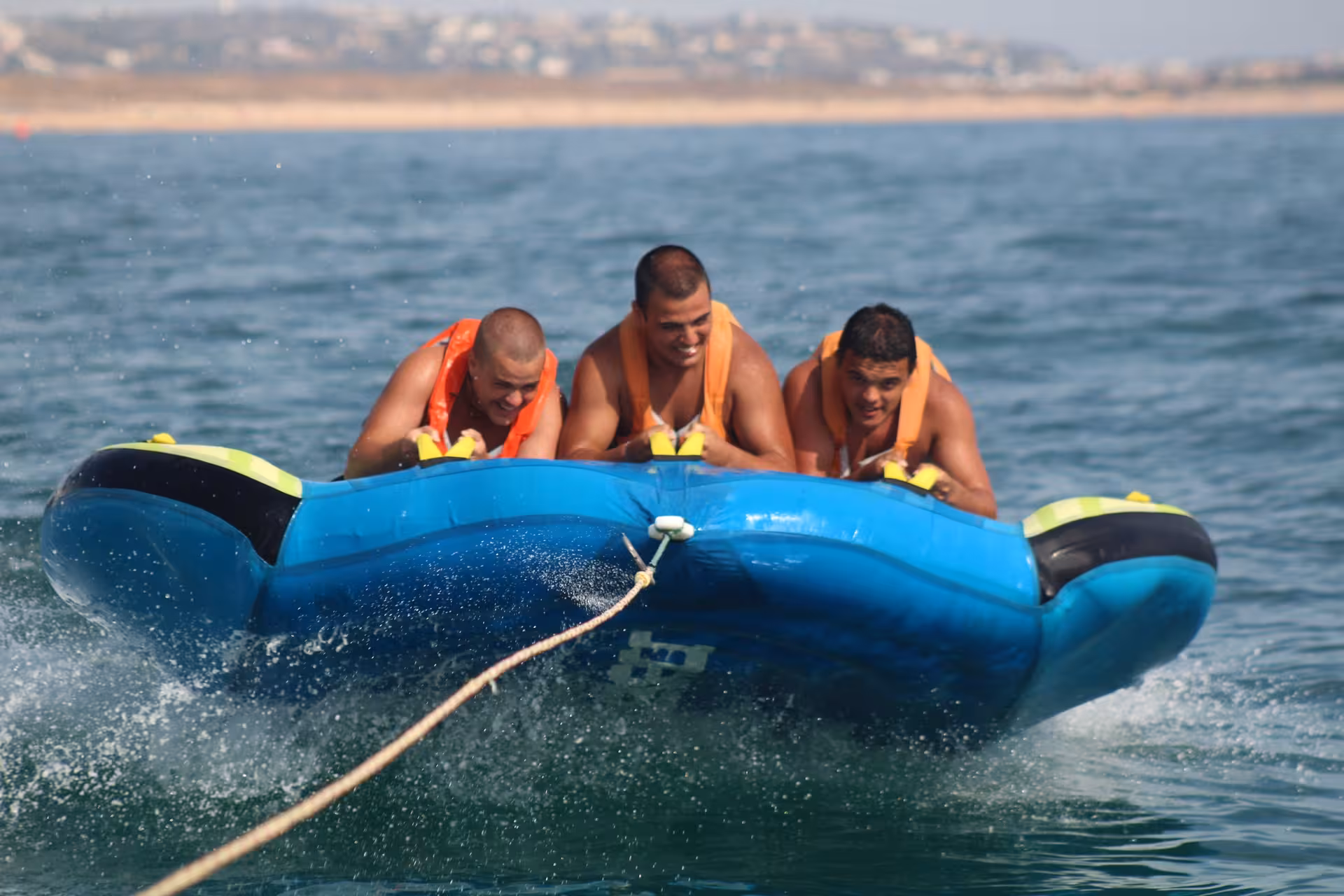 Three guys in life vests holding on tight during an exciting Crazy Cookie inflatable tube ride on open ocean waters