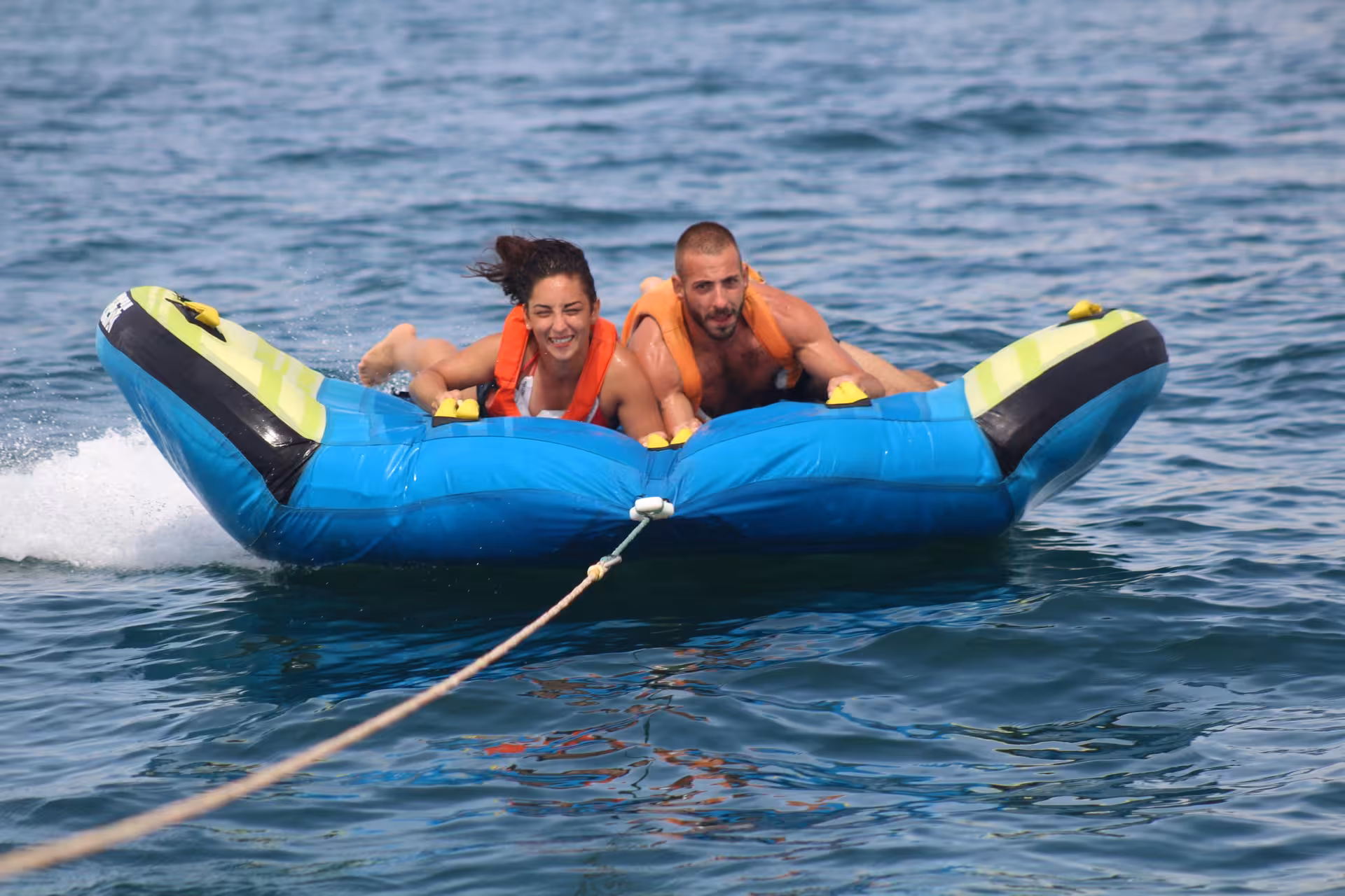 Smiling couple wearing life jackets enjoying a thrilling Crazy Cookie towable tube water adventure on a sunny day