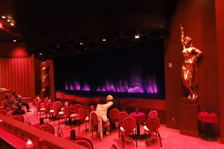 Red-lit Crazy Horse Paris cabaret interior with golden statues, round chairs, and illuminated stage curtain