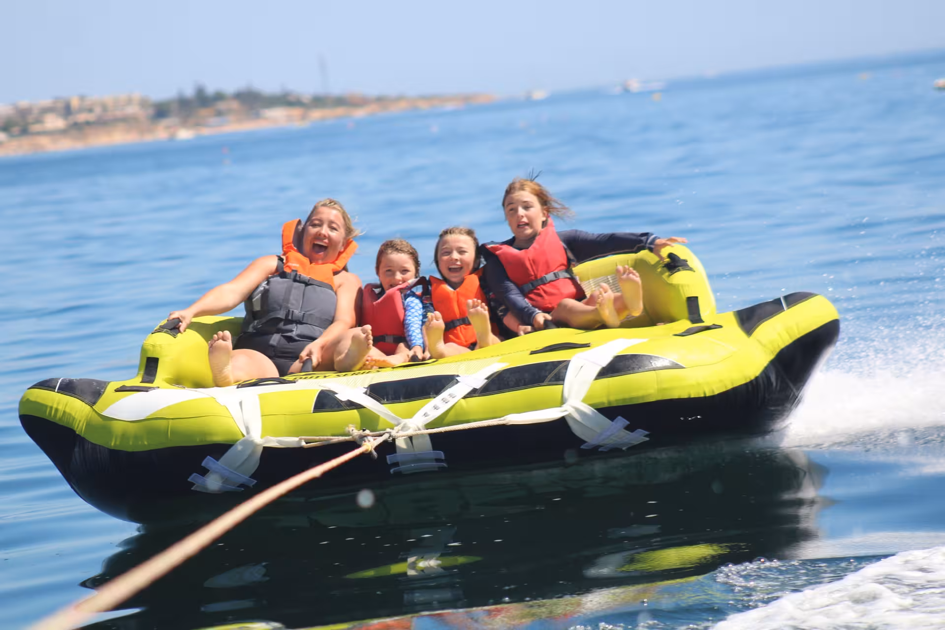 Family with kids in life jackets screaming with joy on a Crazy Sofa towable inflatable ride on sunny ocean waters
