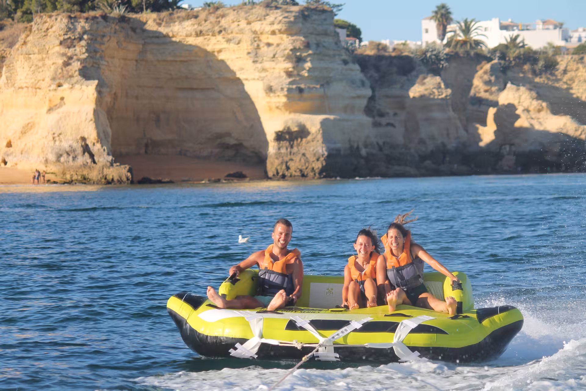 Three friends riding the thrilling Crazy Sofa inflatable towable tube near Algarve's stunning rock cliffs