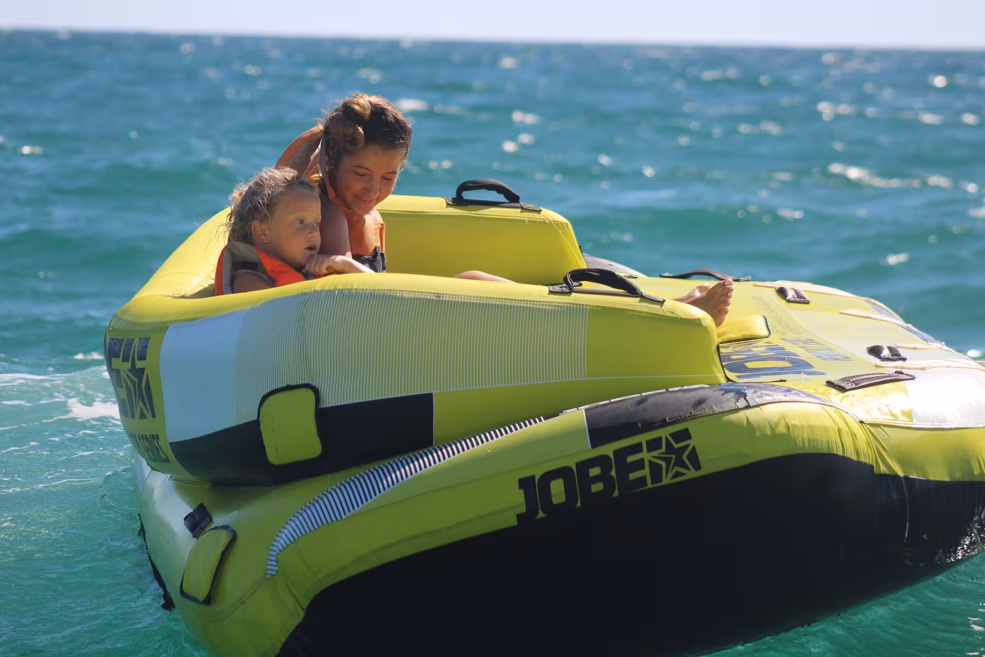 Mother and child enjoying a fun Crazy Sofa Jobe inflatable tube ride on turquoise sea with life jackets on