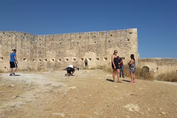 Visitors explore a historic stone fortress under the clear blue sky on the Paths of Old Cretan Life tour from Chania.