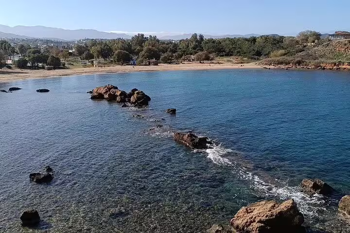 Scenic view of a serene beach in Crete with clear blue waters and rocky outcrops under a bright blue sky.