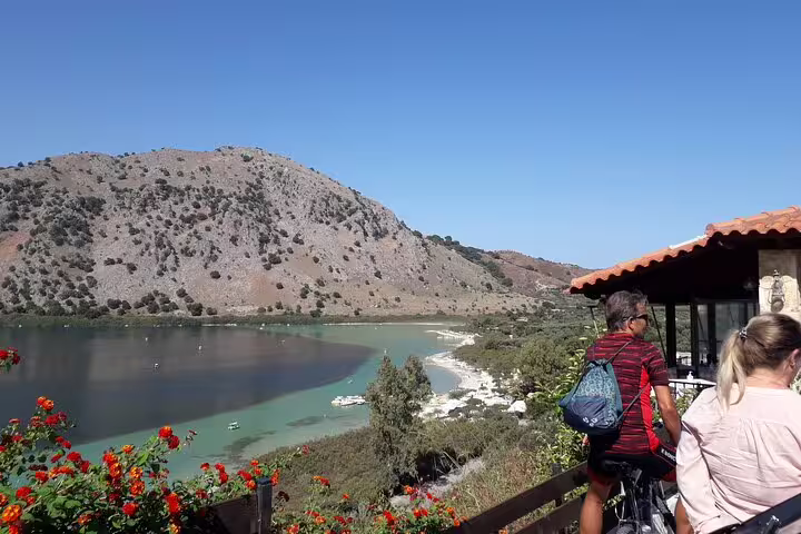 Tourists enjoying panoramic views of serene Lake Kournas surrounded by mountains and vibrant flowers in Crete.