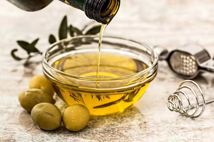 Fresh olive oil being poured into a glass bowl with olives, showcasing Crete's traditional culinary delights.